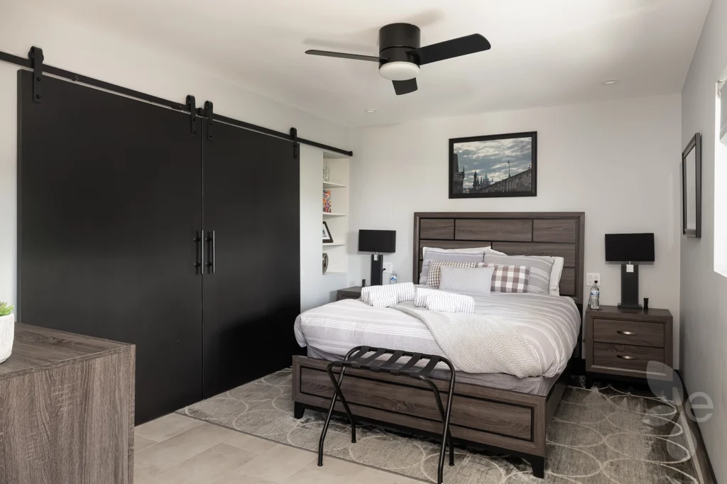 Master suite bedroom with nightstand, lamp, sliding barn door, fan, and built-in shelving.
