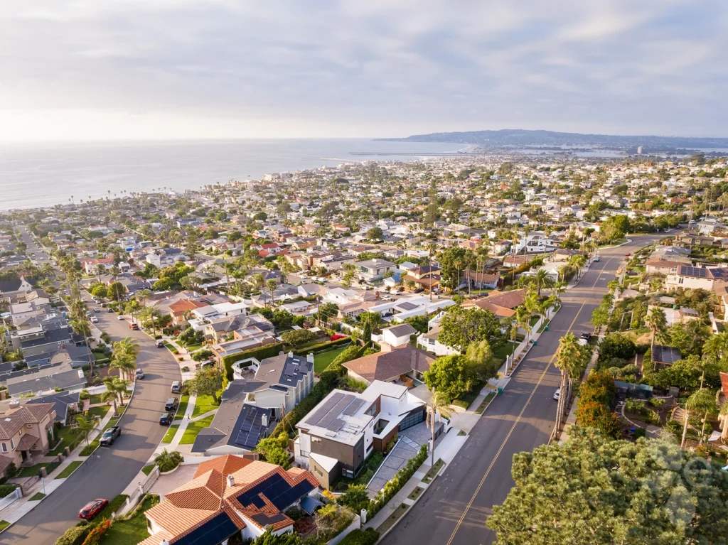 A bird's eye view of a neighborhood with houses and the ocean in the distance.