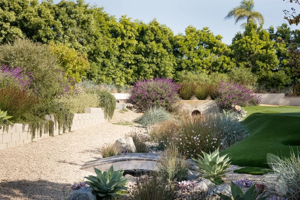 Gravel pathway with wood bridge crossing over to putting green.