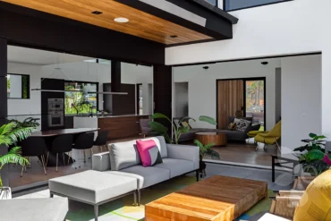 Another view of the Home Interior Living Room with focus on couch and center piece table. There is a view of the kitchen in the background as well where you can see the stove and Island.