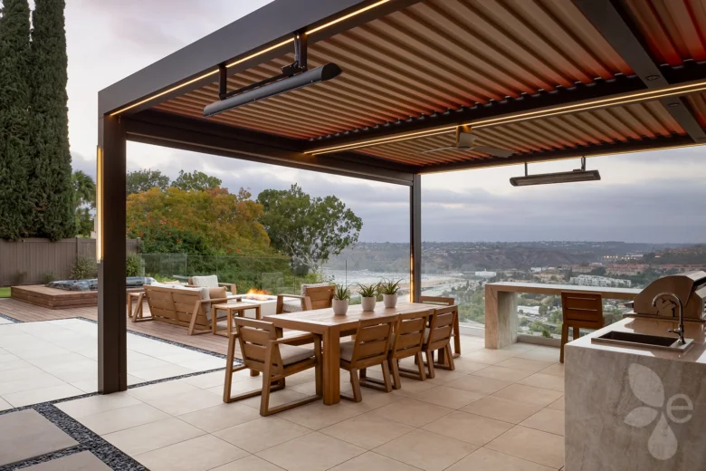 Cliffside outdoor kitchen with dining table, under a pergola, with a hot tub, lounge, and fire pit in the background.