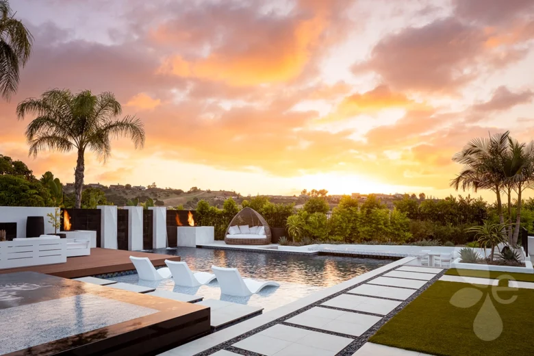 A zoomed out sunset shot behind surrounding Tropical Landscape with seating on a water feature near the pool with a fire feature and hammock across the pool