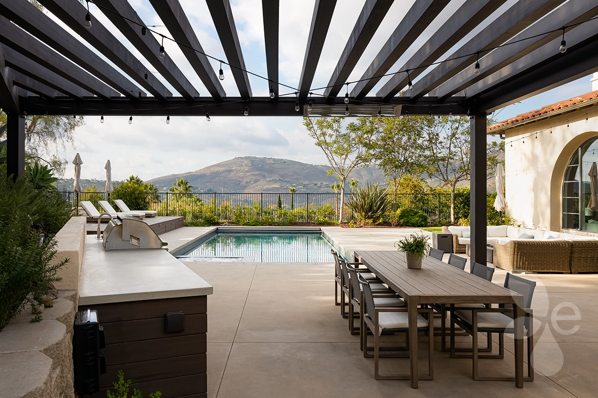 Outdoor kitchen and dining table under pergola, overlooking pool and the local canyon.