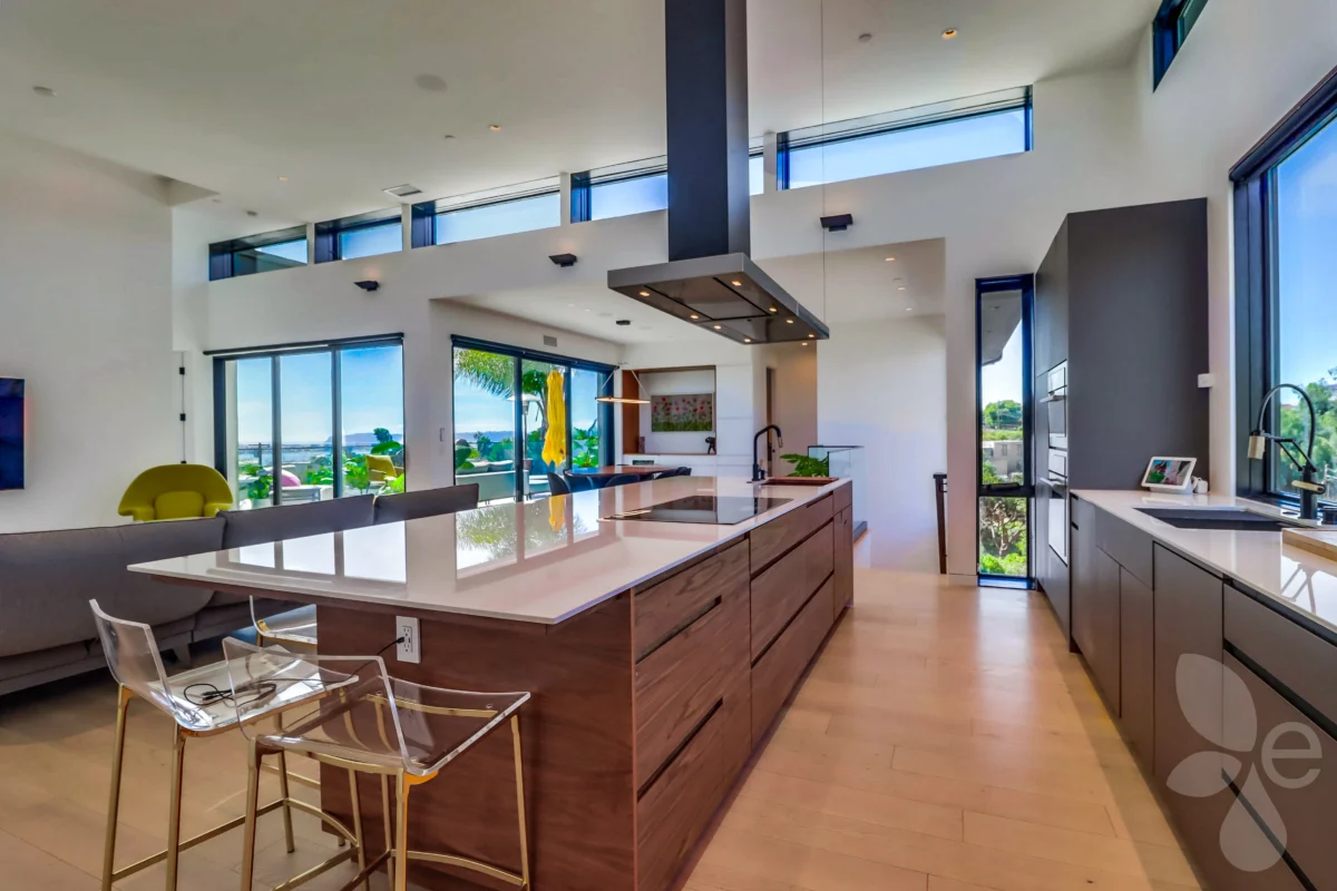 Full kitchen island, including sink, grill, and fridge, with living room in the background.