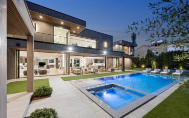 Stunning backyard of a whole home remodel featuring a modern pool and jacuzzi, surrounded by lounge chairs and an expansive outdoor seating area. The remodeled two-story home boasts large glass windows, sleek architecture, and open-concept indoor-outdoor living spaces, creating a luxurious and seamless flow.