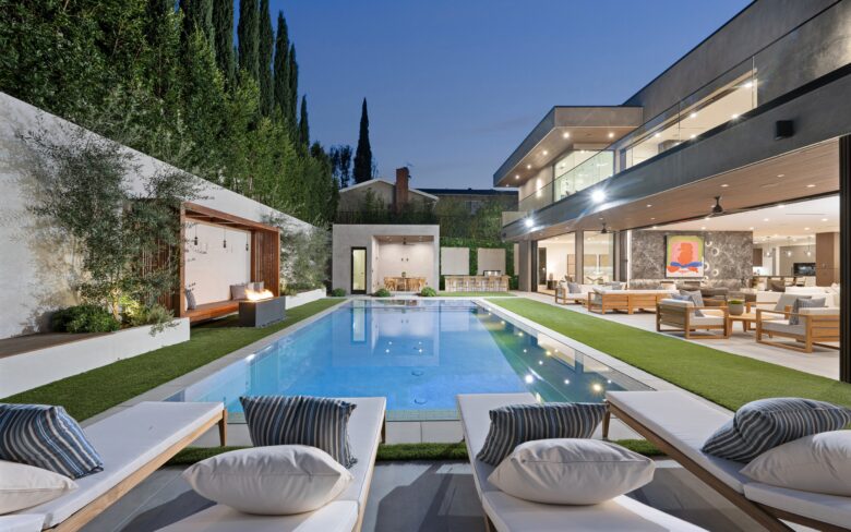 Luxurious modern backyard of a whole home remodel, featuring a sleek swimming pool, lounge chairs, a cozy fire pit, and contemporary outdoor seating areas. The remodeled two-story home showcases large glass windows, minimalist design, and a seamless indoor-outdoor living space.